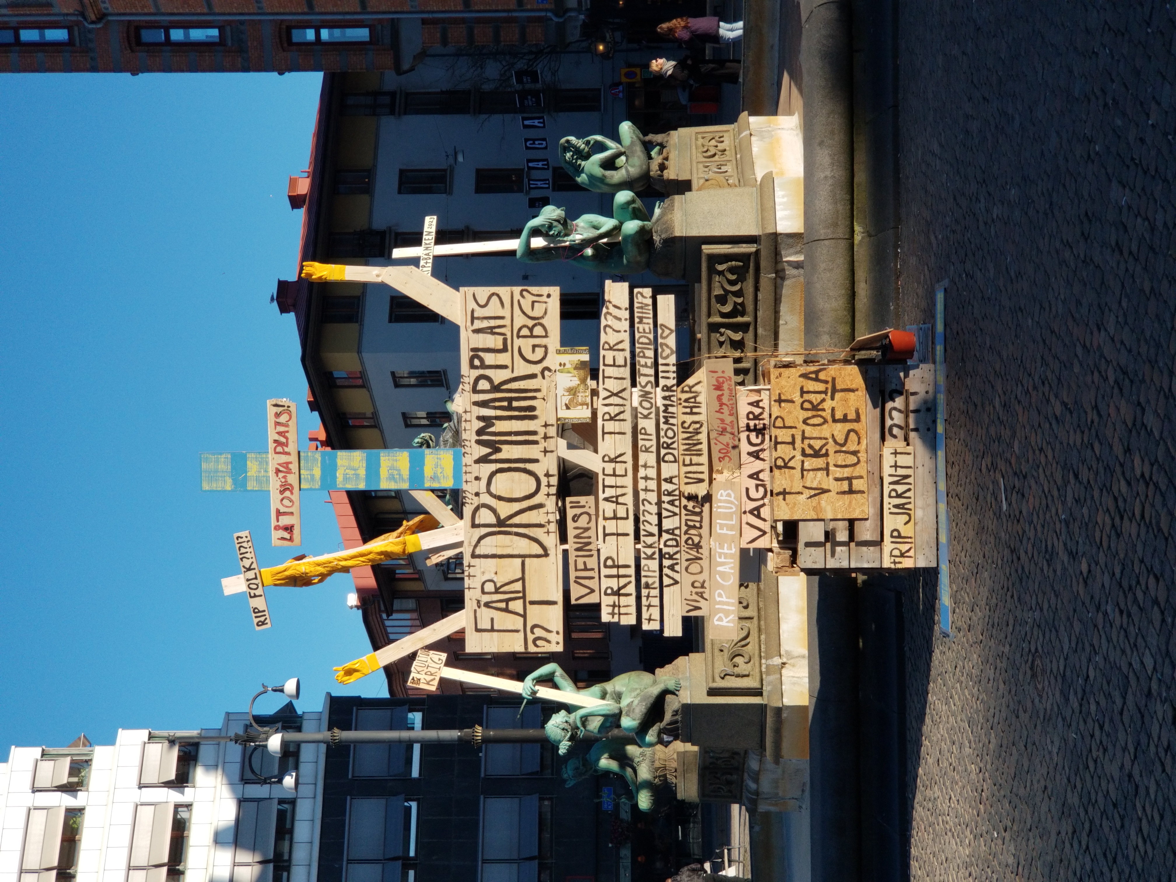 Large public sculpture of stacked wooden pallets and protest signs. Stor offentlig skulptur av staplade träpallar och protestskyltar.