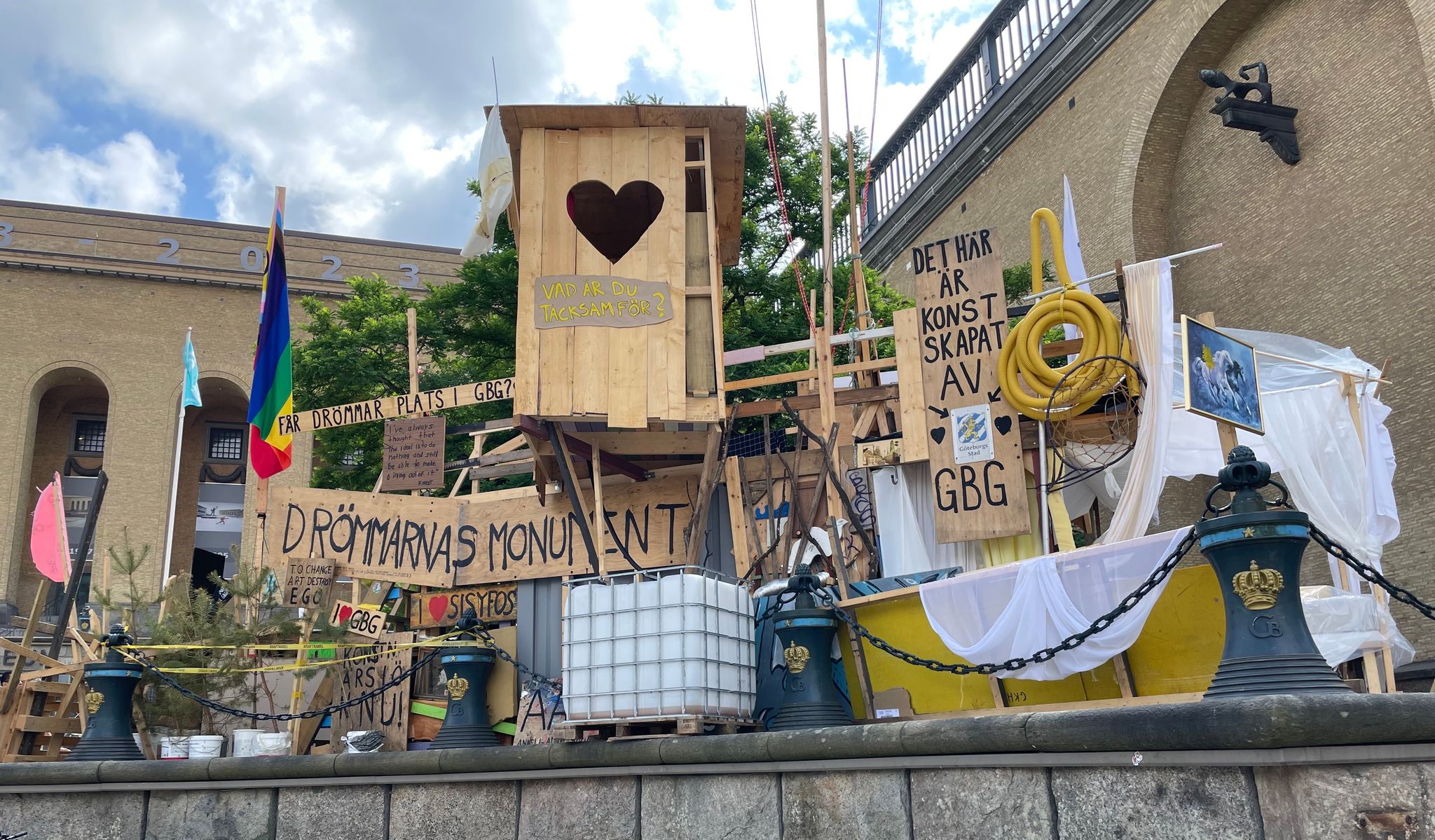 Large outdoor assemblage of reclaimed wood, signs, and fabric. Stor utomhusinstallation formad av trä, skyltar och tyg.