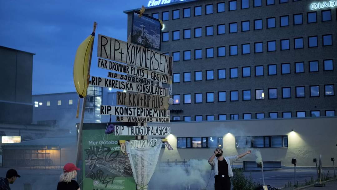 Large wooden protest sign with cardboard RIP messages and a plastic banana, surrounded by smoke. Stor protestskylt i trä och kartong omgiven av rök.