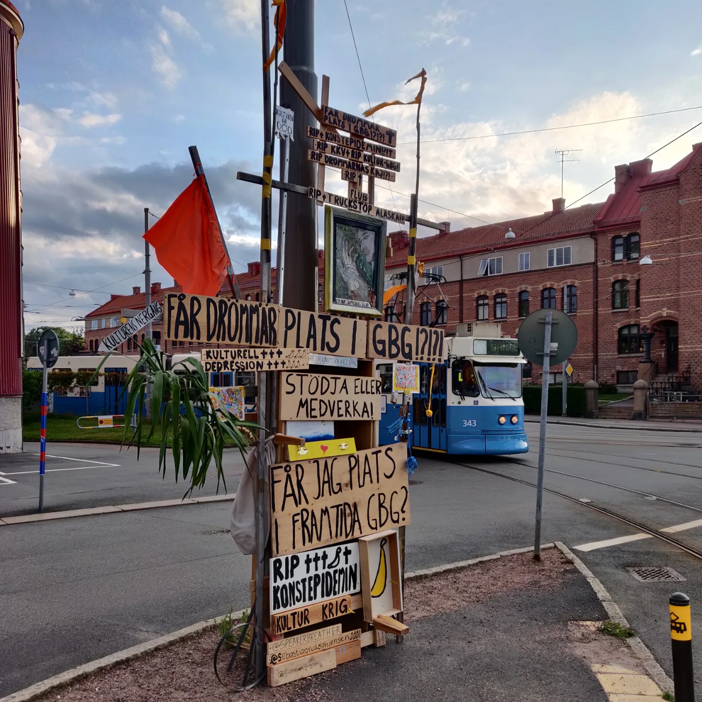 A tall street art totem of scrap wood signs and a red flag. En hög gatukonst-totempåle byggd av träskyltar i ett gathörn.