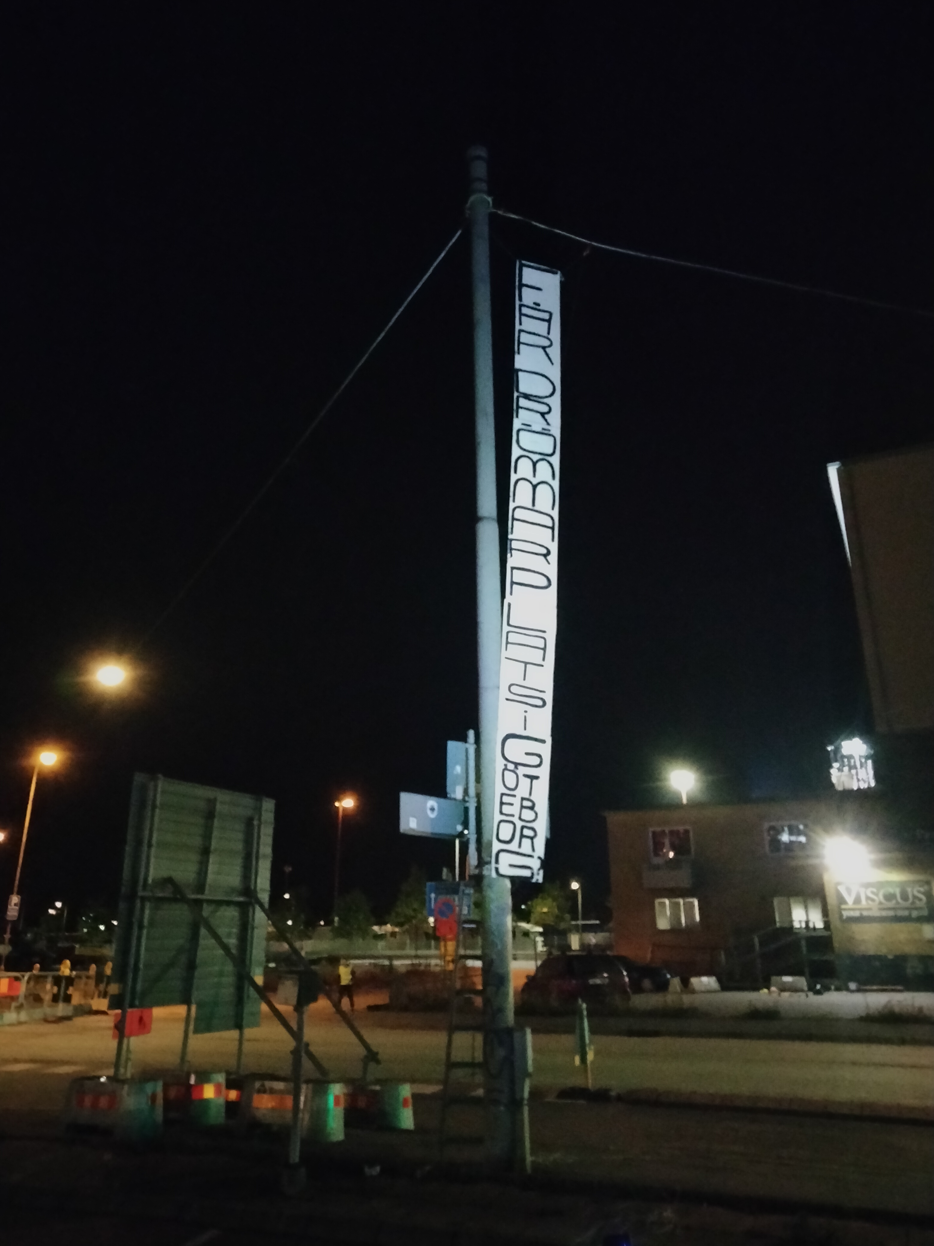 Tall white fabric banner on a night pole reading FAR DRÖMMAR PLATS. Lång vit tygvepa på en lyktstolpe med text om drömmar i Göteborg.