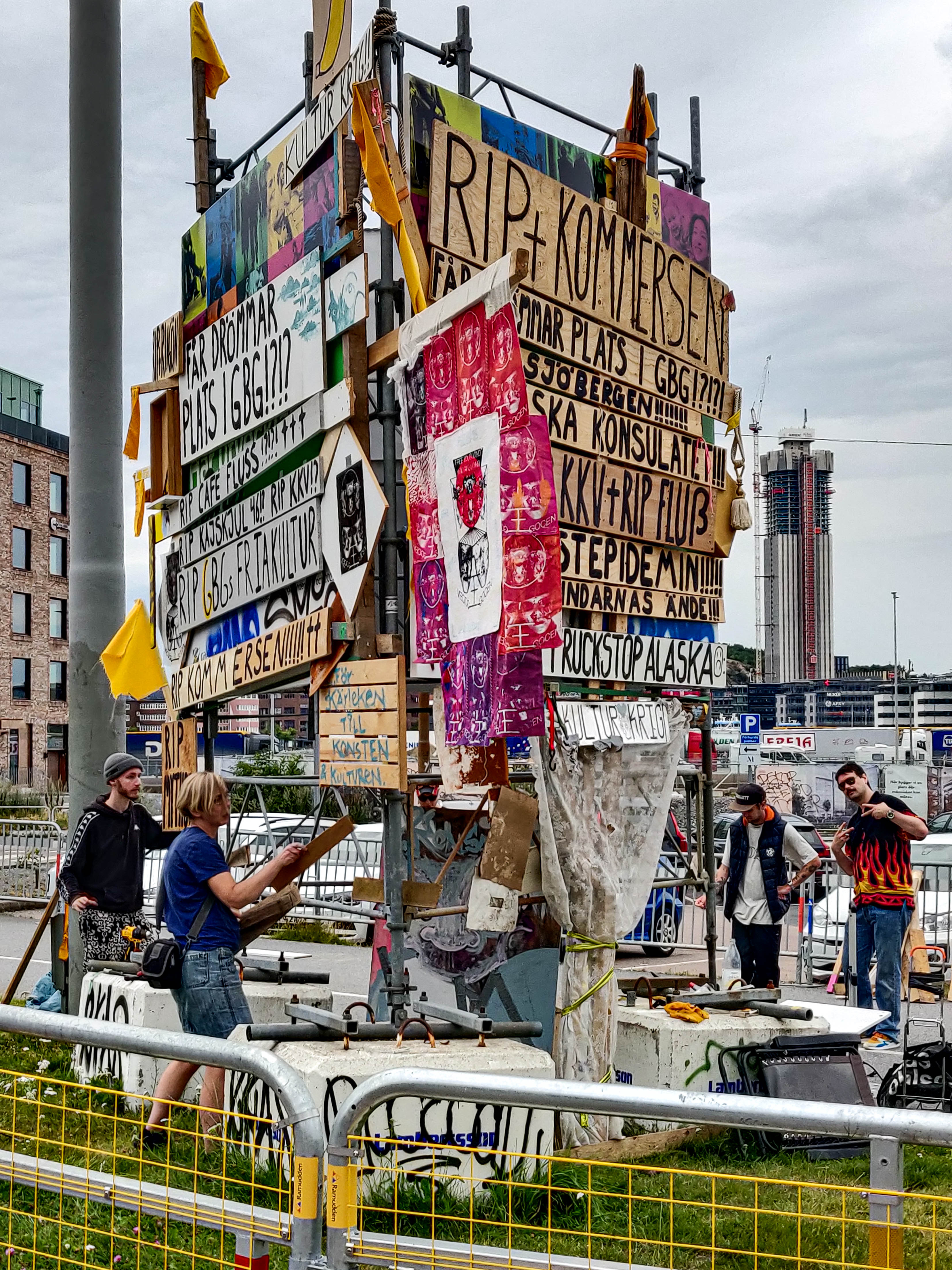 Large scaffolding tower covered in painted wooden signs and fabric. Stort torn av byggställningar täckt med målade träskyltar och tyg.